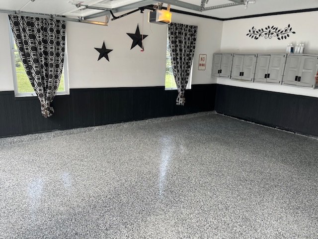 Clean, organized garage with speckled epoxy floor, star wall decorations, patterned curtains, and wall cabinets.