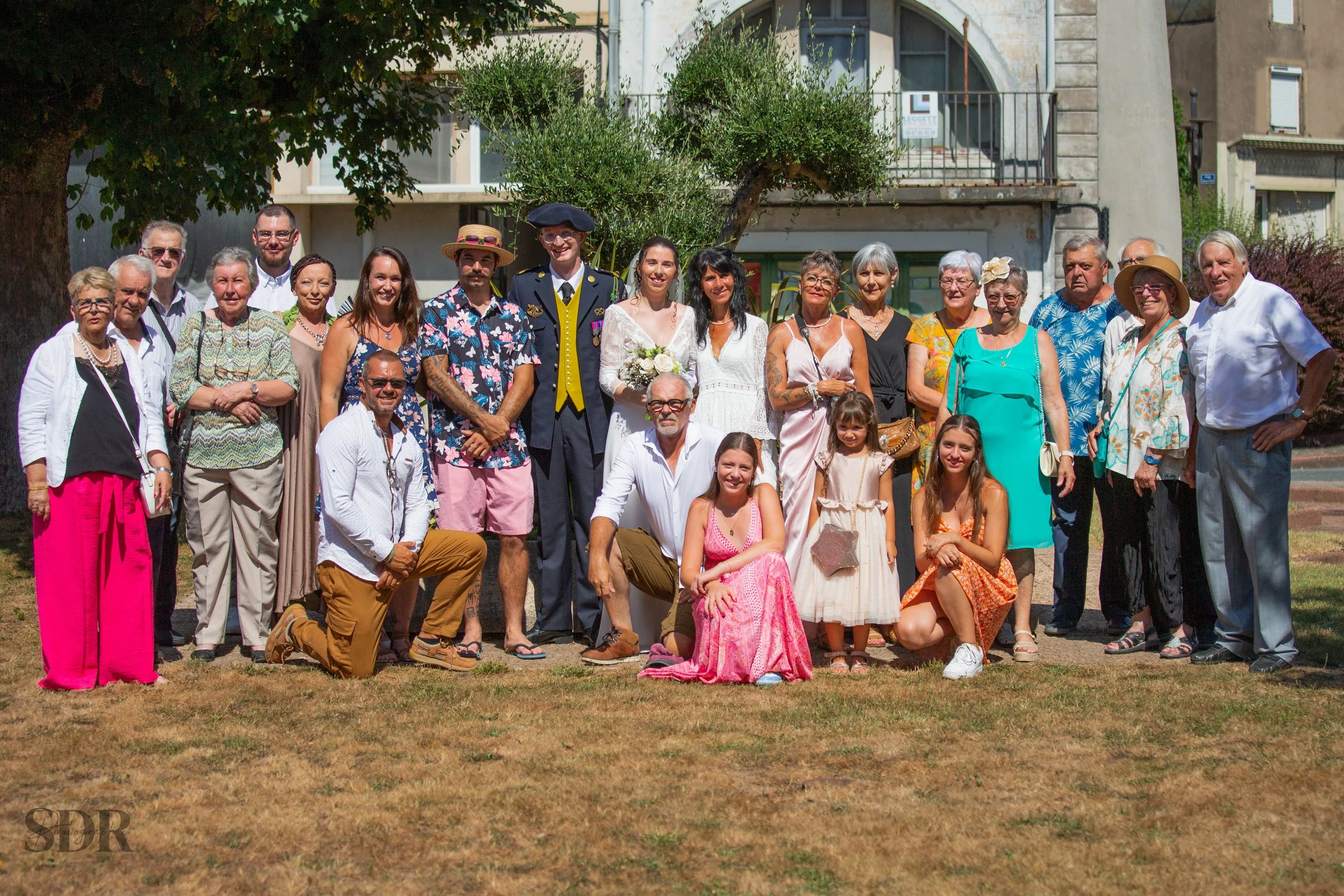 Groupe de personnes habillées pour une occasion spéciale, posant ensemble à l'extérieur, probablement lors d'une cérémonie ou d'une célébration.