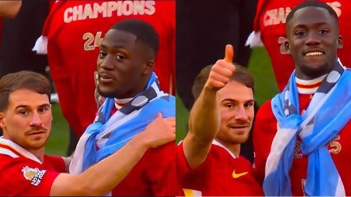 Two soccer players in red jerseys celebrating a championship with a blue and white flag.