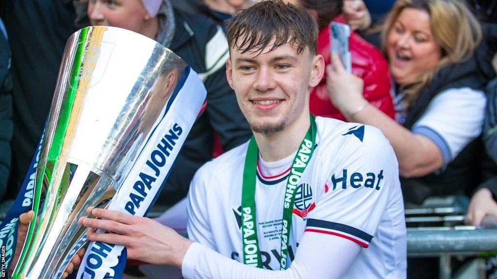 Soccer player holding Papa John's trophy with fans in the background.