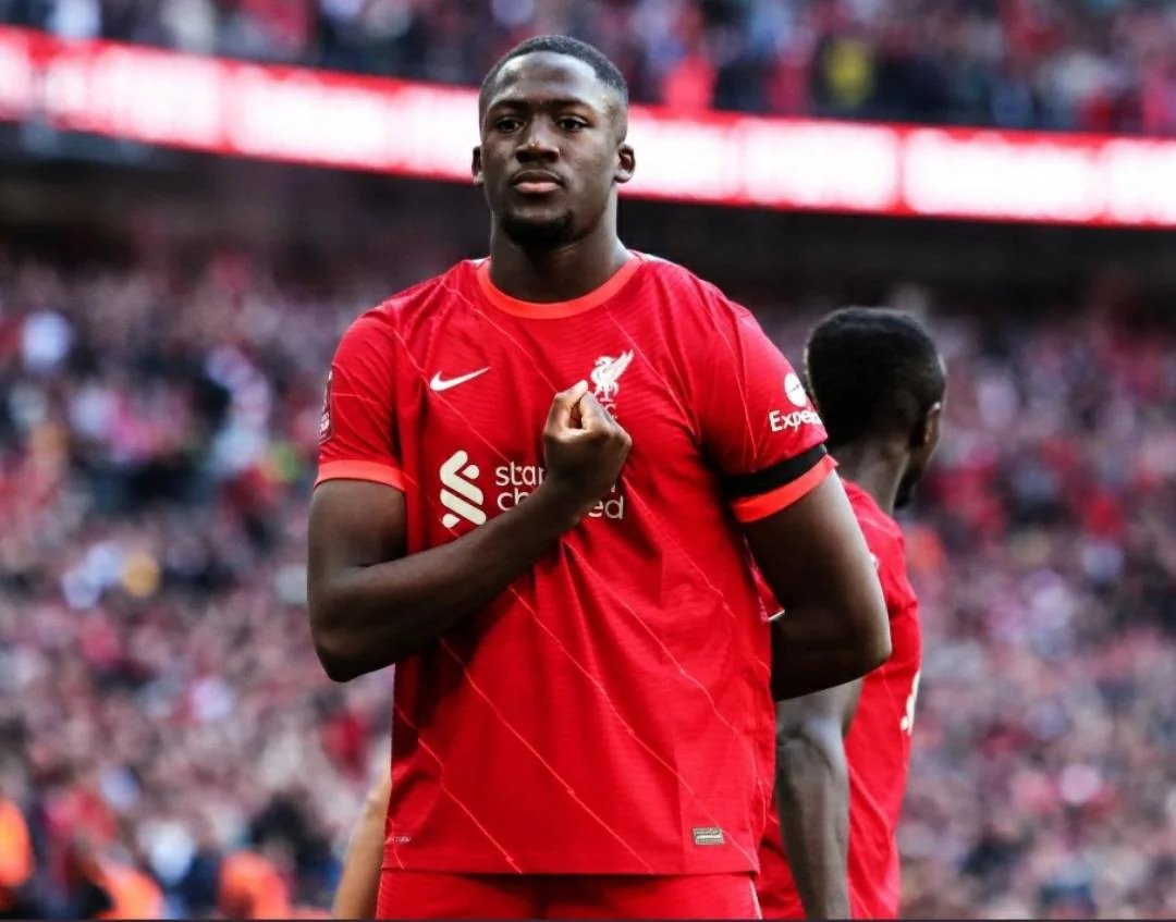 Soccer player in a red Liverpool jersey with a blurred stadium background.