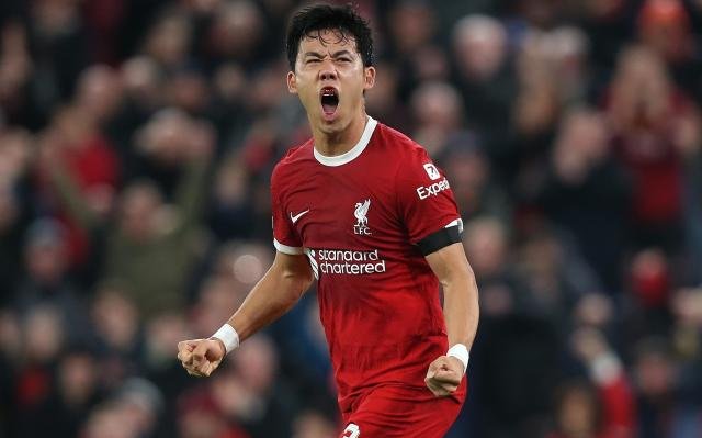 Soccer player in red Liverpool jersey celebrating on the field with a cheering crowd in the background.