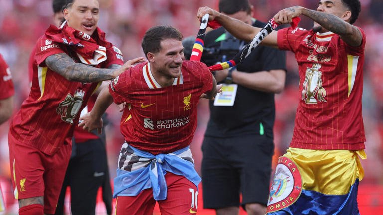 Soccer players celebrating victory in Liverpool jerseys, on a football field adorned with team scarves and flags.