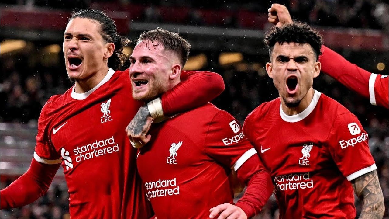 Three soccer players in red Liverpool jerseys celebrating during a match.