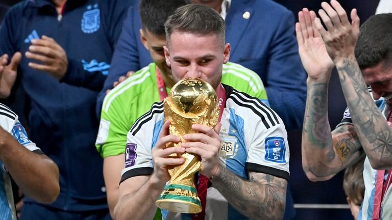Soccer player kissing World Cup trophy with teammates celebrating