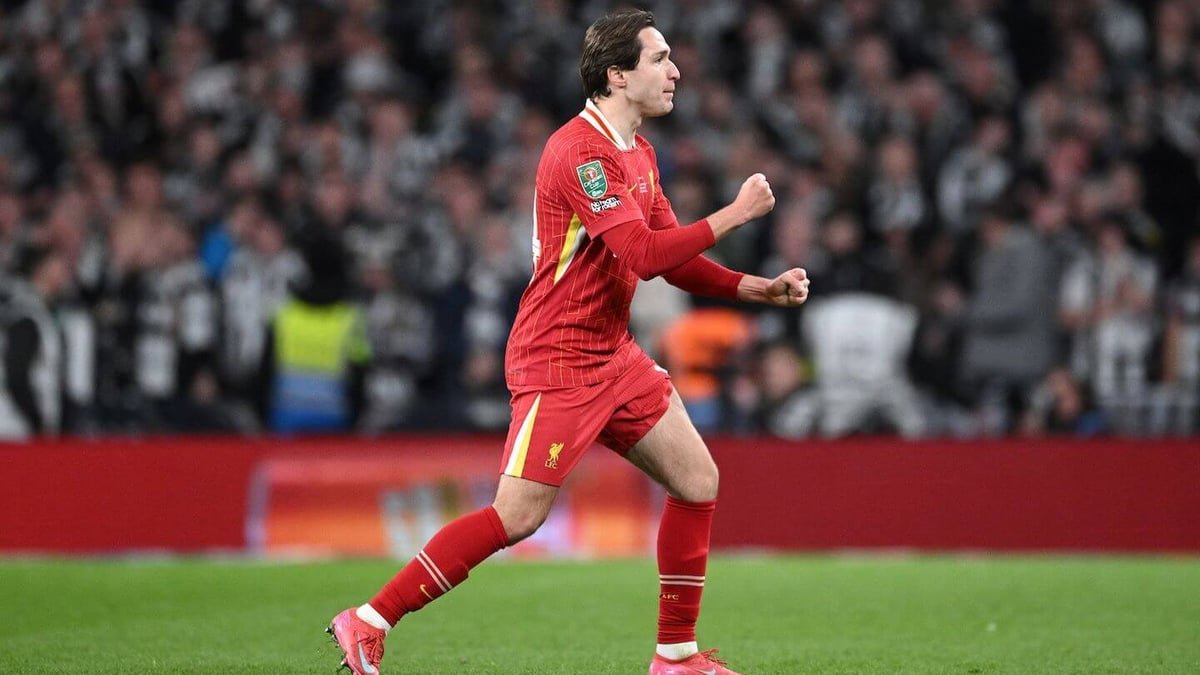 Soccer player in red Liverpool uniform celebrates on field with crowd in background.