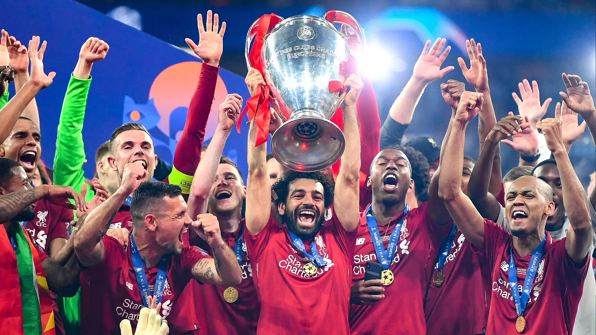 Soccer players in red jerseys celebrating with a trophy.