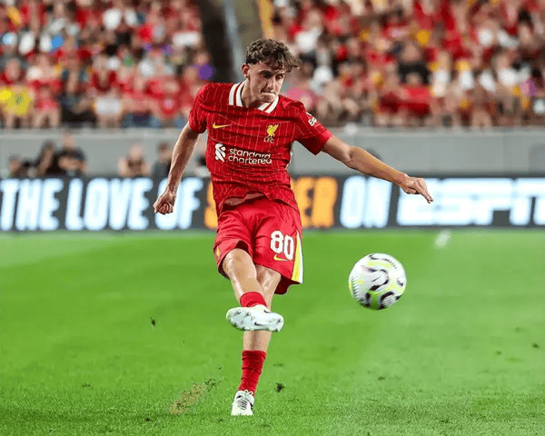 Soccer player in a red uniform kicking a soccer ball on a field with a crowd in the background.