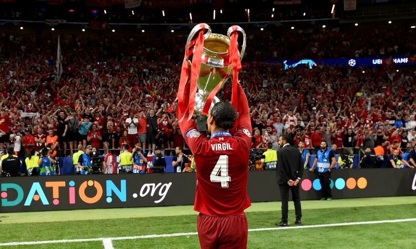 Soccer player holding a trophy in a stadium, celebrating victory with fans in the background.