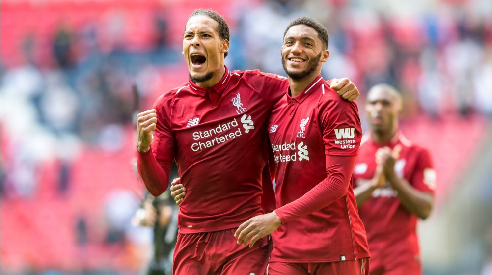 Two soccer players in red Liverpool jerseys celebrating on the field, with one player jubilantly raising his fist.