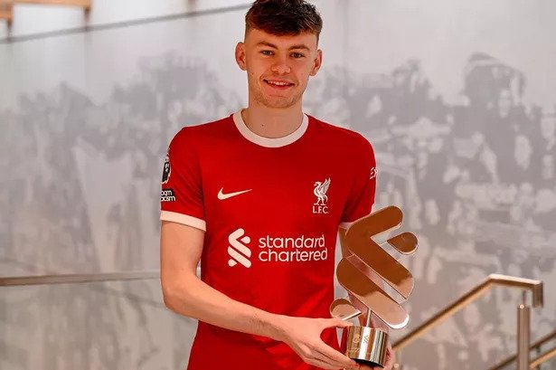 Person holding a trophy while wearing a red Liverpool FC jersey.