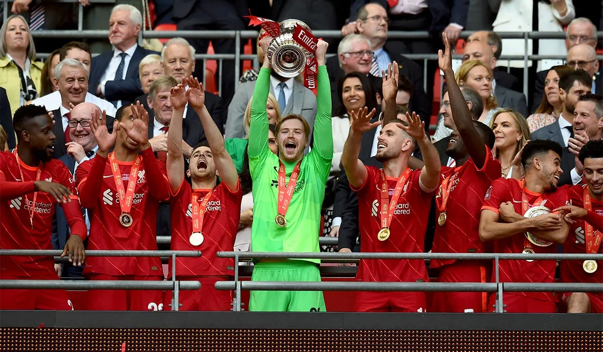 Soccer team celebrating trophy win with medals and fans in background.