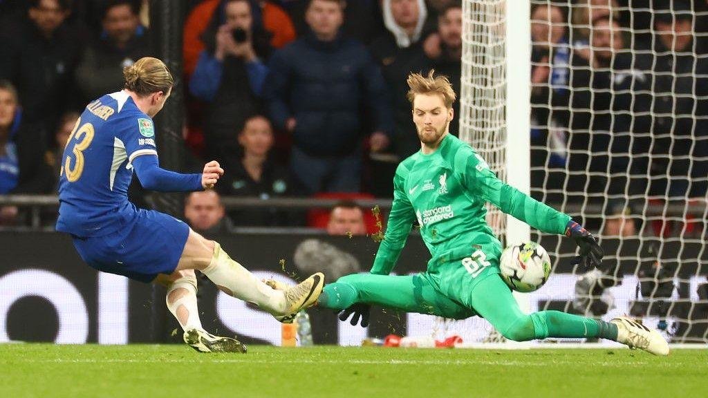 Soccer player in blue about to kick the ball past a goalkeeper in green, during a match.