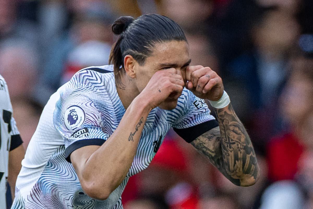 A soccer player in a white and black jersey making a celebration gesture by placing his hands near his eyes, mimicking glasses. The jersey has a Premier League logo on the sleeve, and the player has tattoos on his arms.