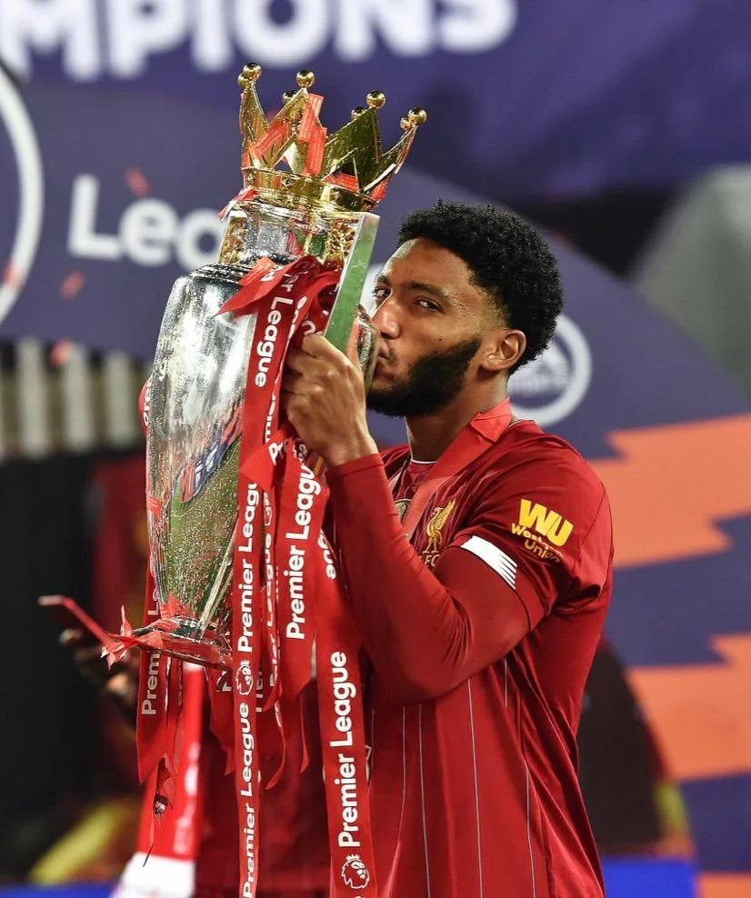 Soccer player in red jersey kissing Premier League trophy.