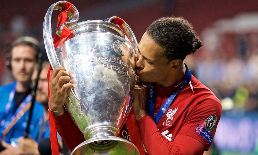 A soccer player in a red jersey kisses the UEFA Champions League trophy on the field.