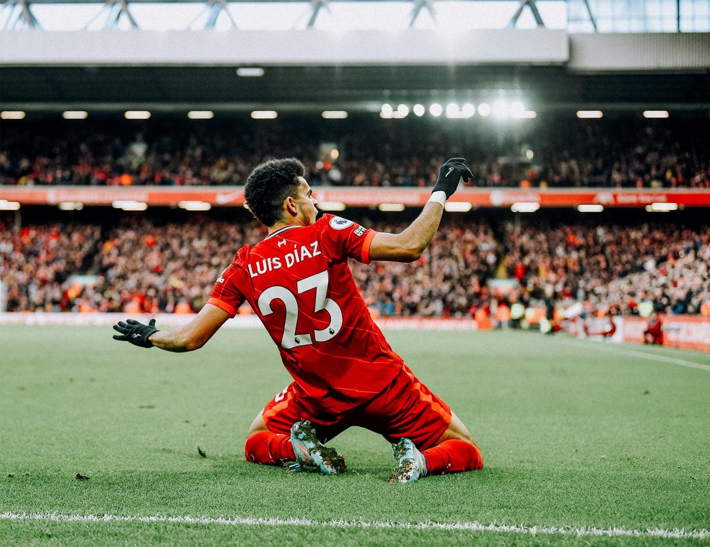 Soccer player in red jersey sliding on the field in celebration with a cheering crowd in the background.