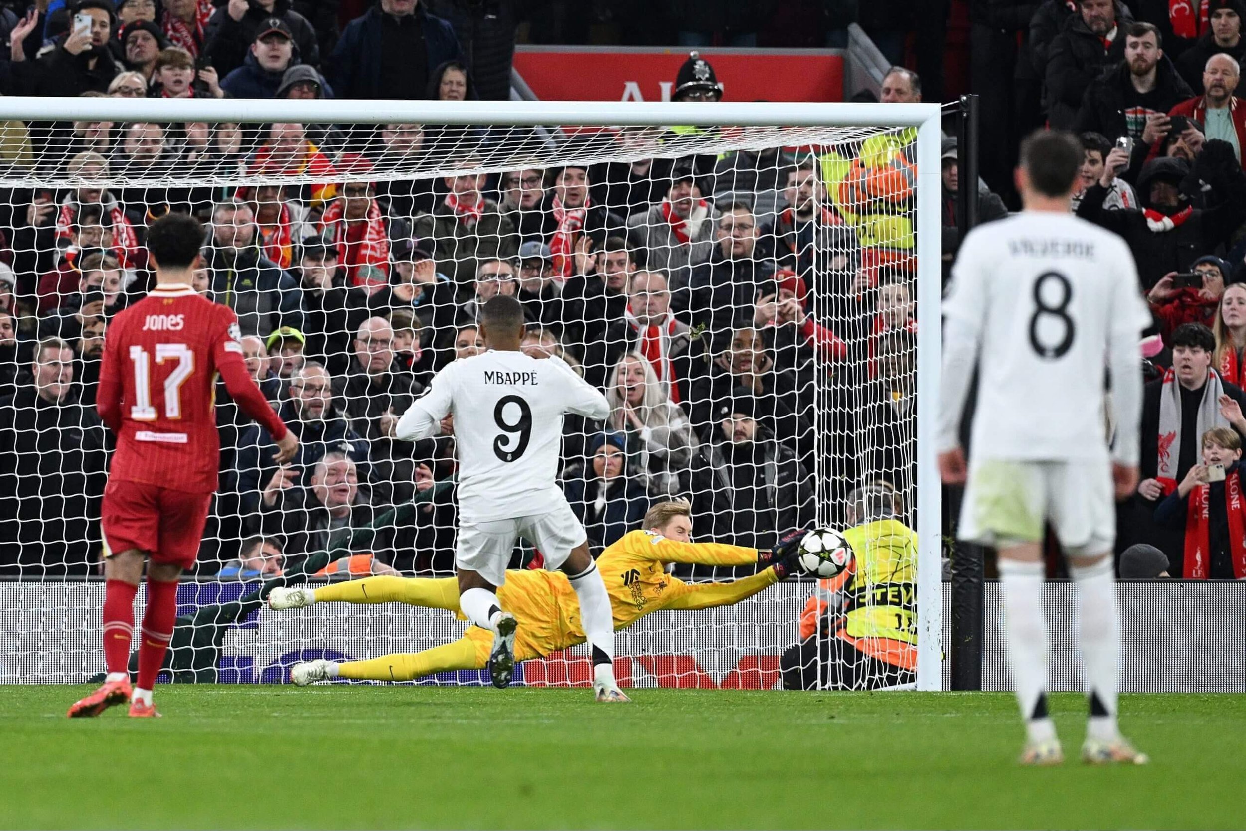 Soccer match with goalkeeper saving a shot, player in white, crowd in background.