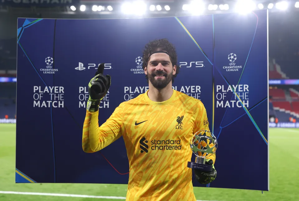 Soccer player in a yellow Liverpool FC uniform holding a trophy with "Player of the Match" background at a stadium.