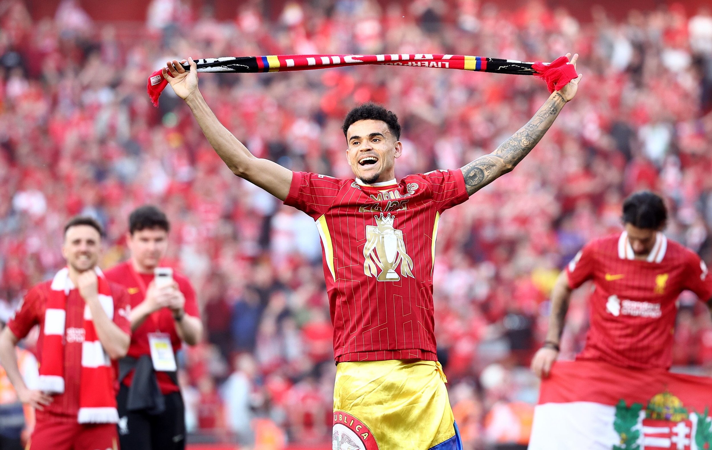 Soccer player celebrating with a scarf; wearing a red jersey and yellow shorts, with a crowd in the background.