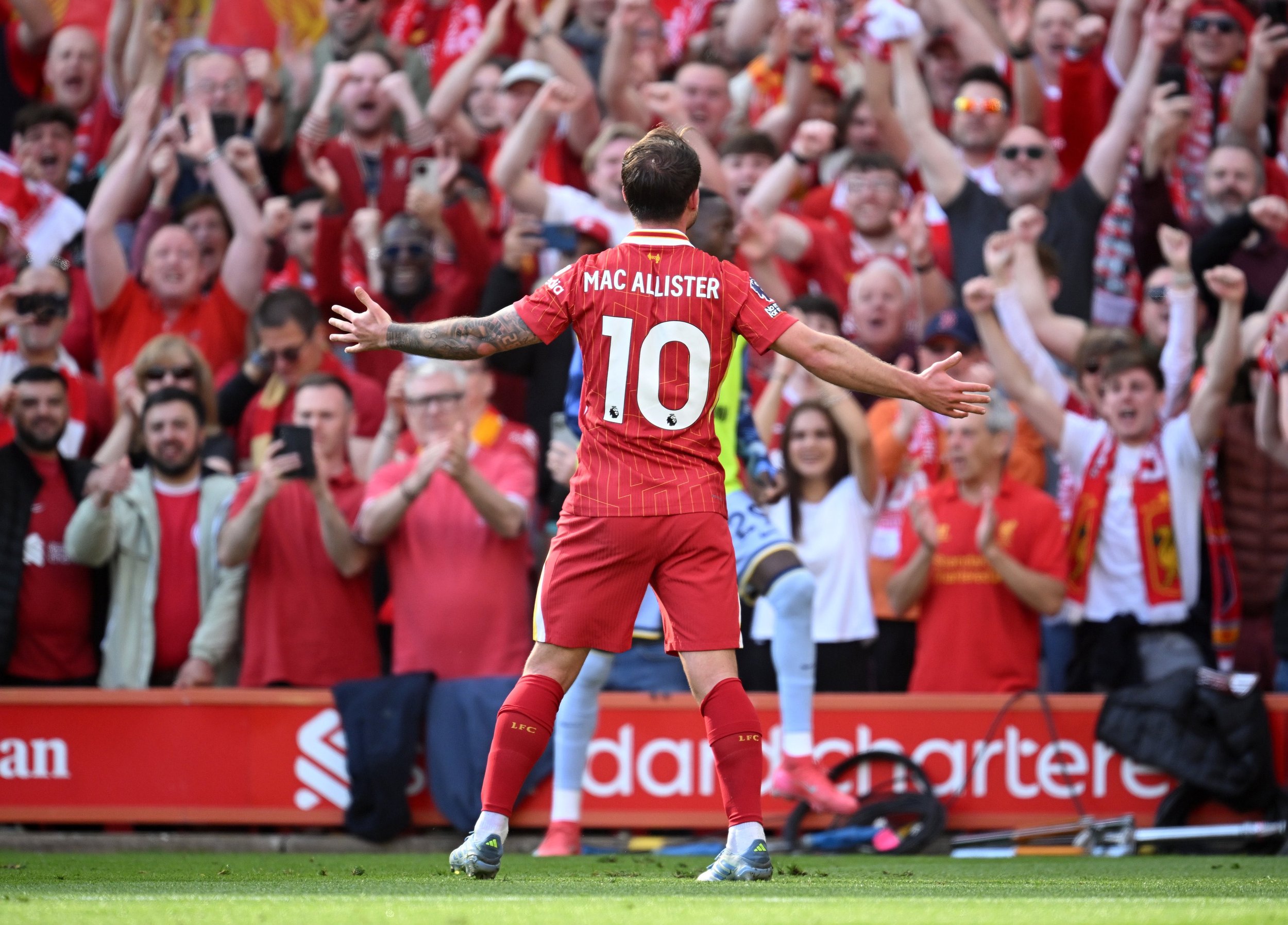 Soccer player wearing a red jersey with number 10 celebrates in front of cheering fans at a stadium.