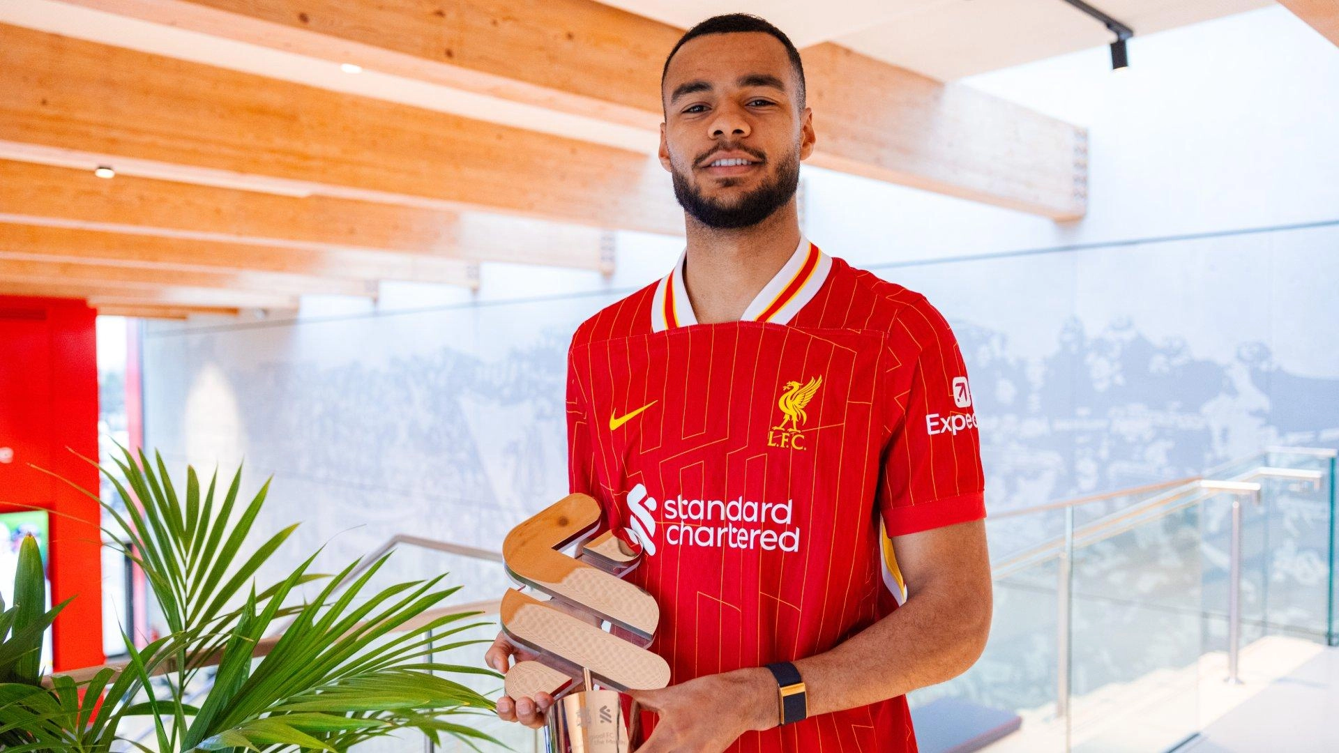 A person in a red Liverpool FC jersey holding a sports trophy indoors.