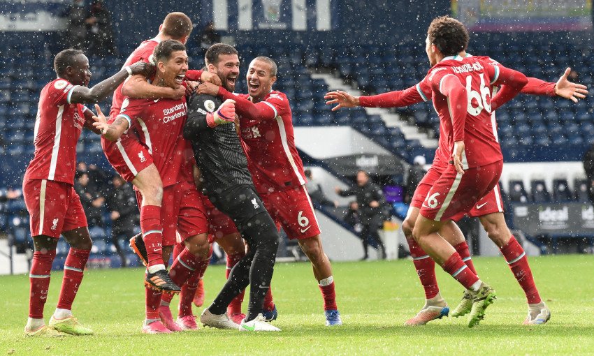 Soccer players in red uniforms celebrating a goal on a wet field, embracing each other enthusiastically.