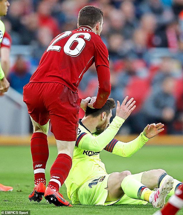Soccer players during a match, one in a red jersey with number 26 helping another player in a neon green jersey who is sitting on the ground.
