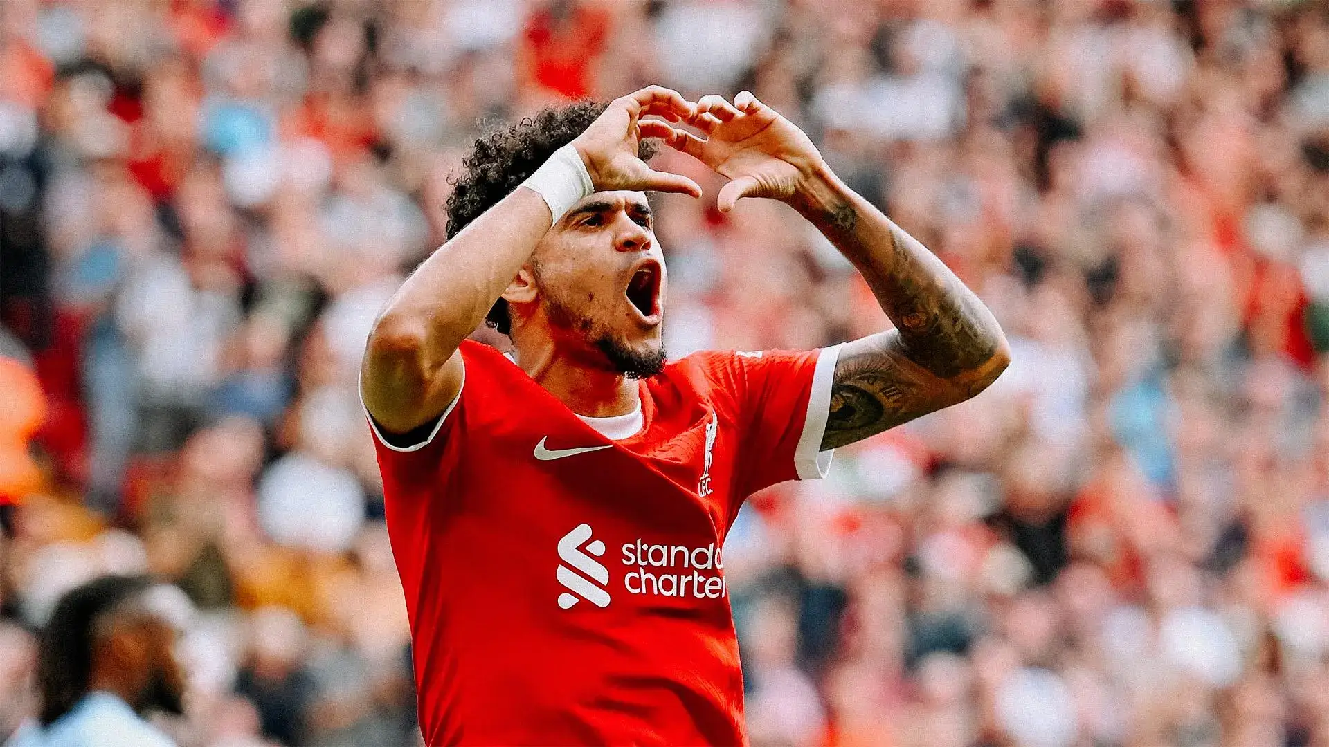Soccer player in red jersey celebrating with a hand gesture forming a heart shape.