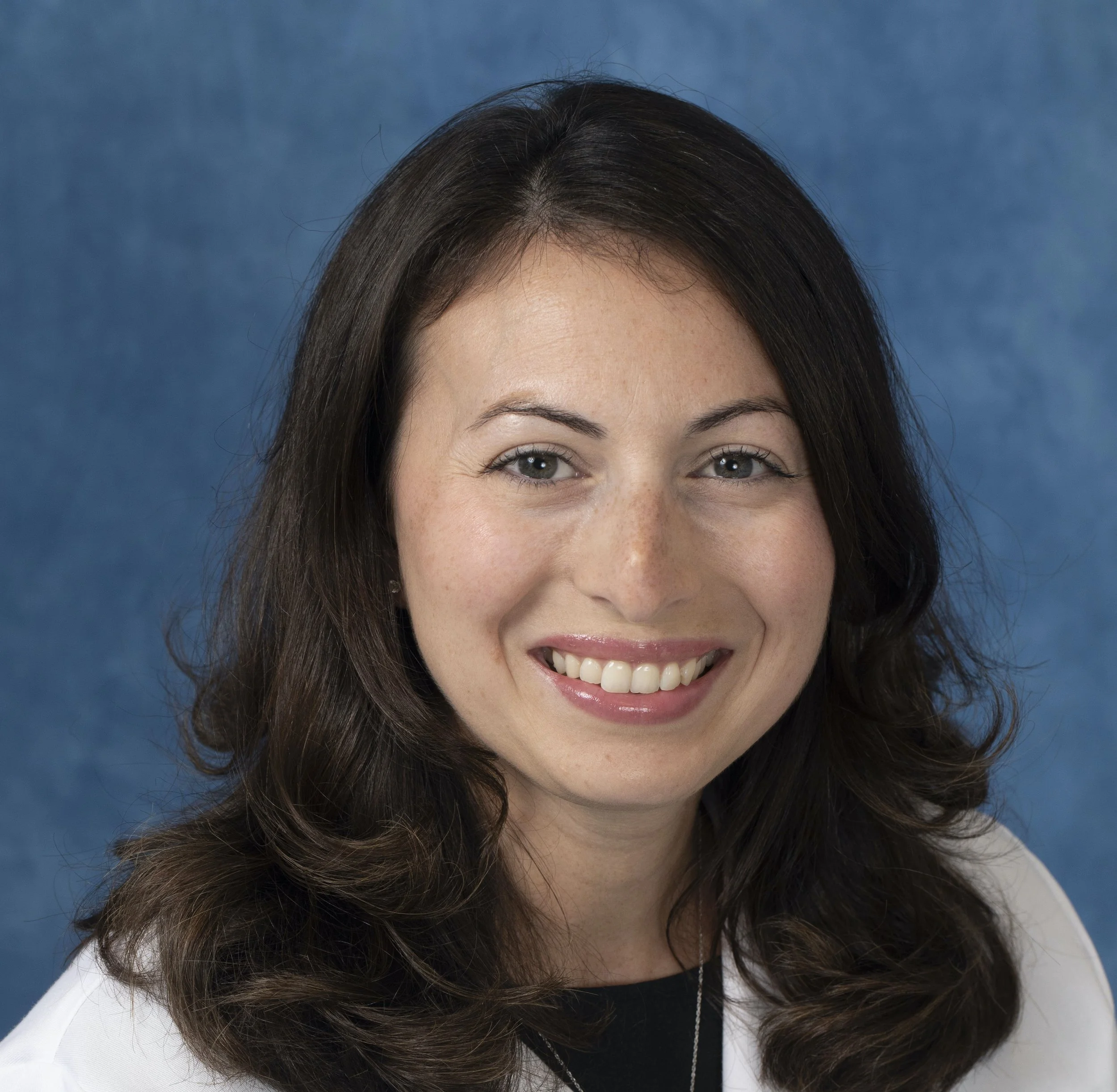 Close-up of a woman with long dark hair, smiling, against a blue background.