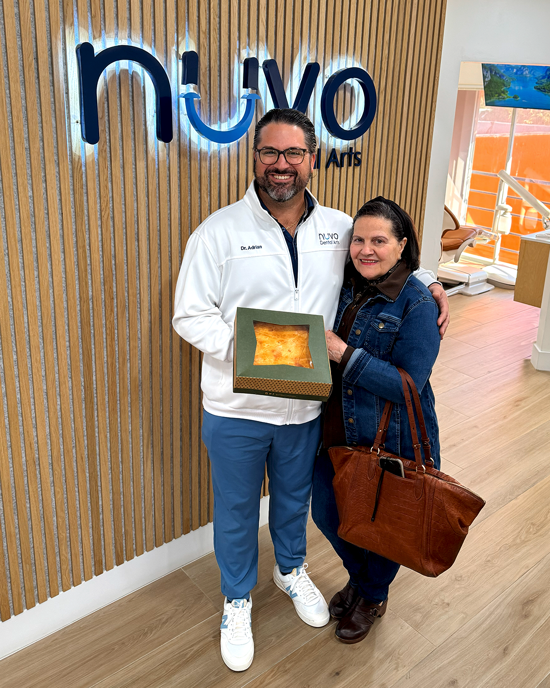Dr. Adrian smiling with a patient offering a small cake as a gesture of gratitude at Nuvo Dental Arts