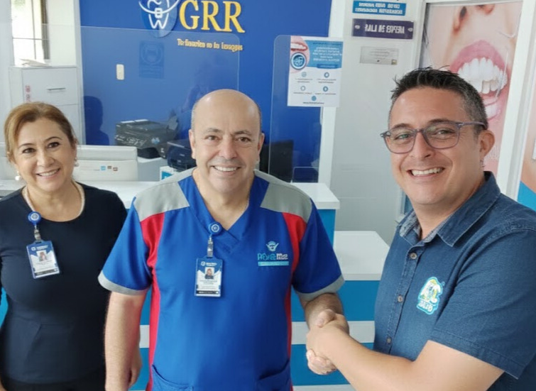 Tres personas en una oficina de servicios, una mujer y dos hombres, con sonrisas, una de las cuales está estrechando la mano del otro.