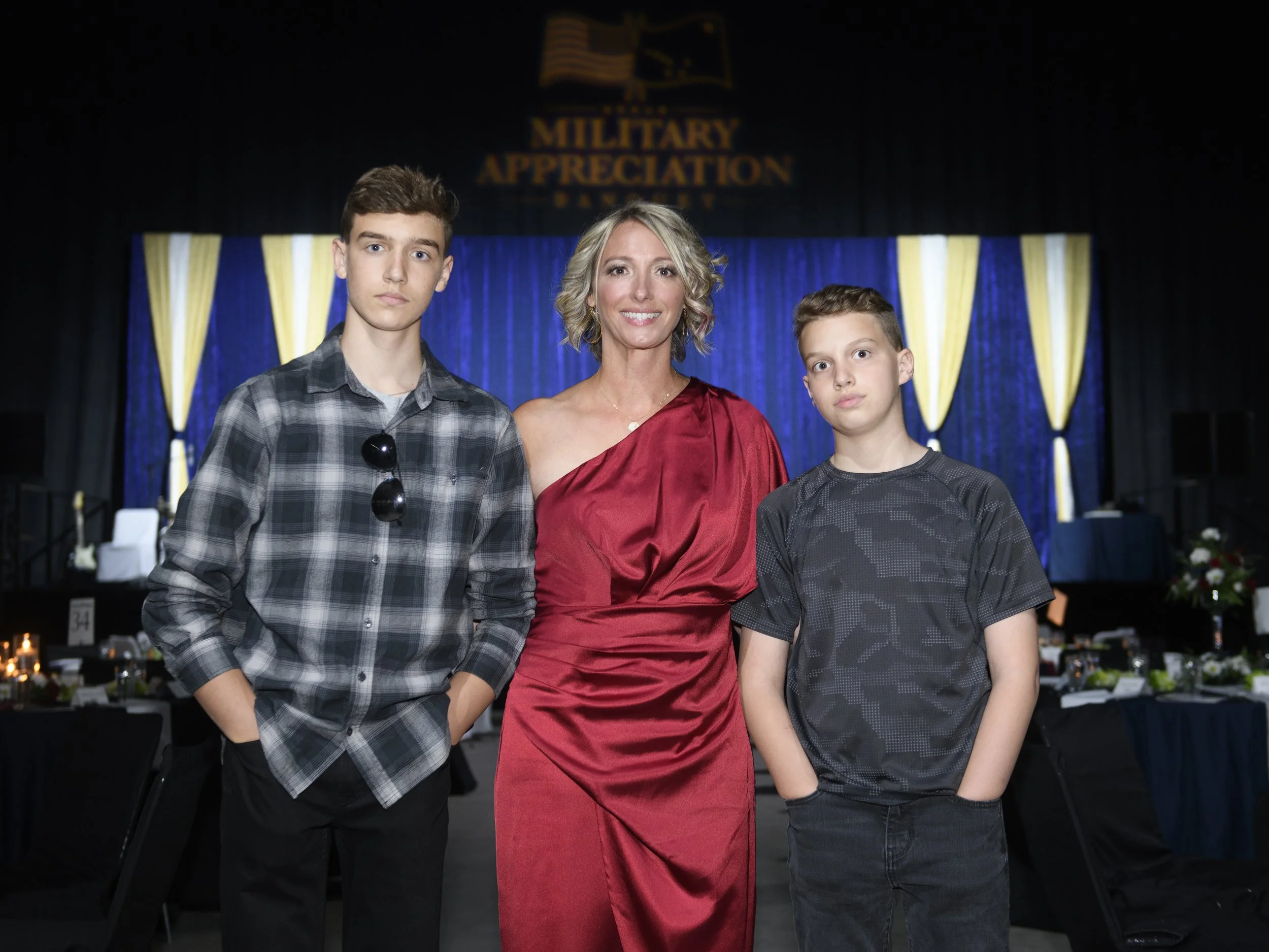 Jennifer in a formal red dress and two young boys on either side of her at a conference.