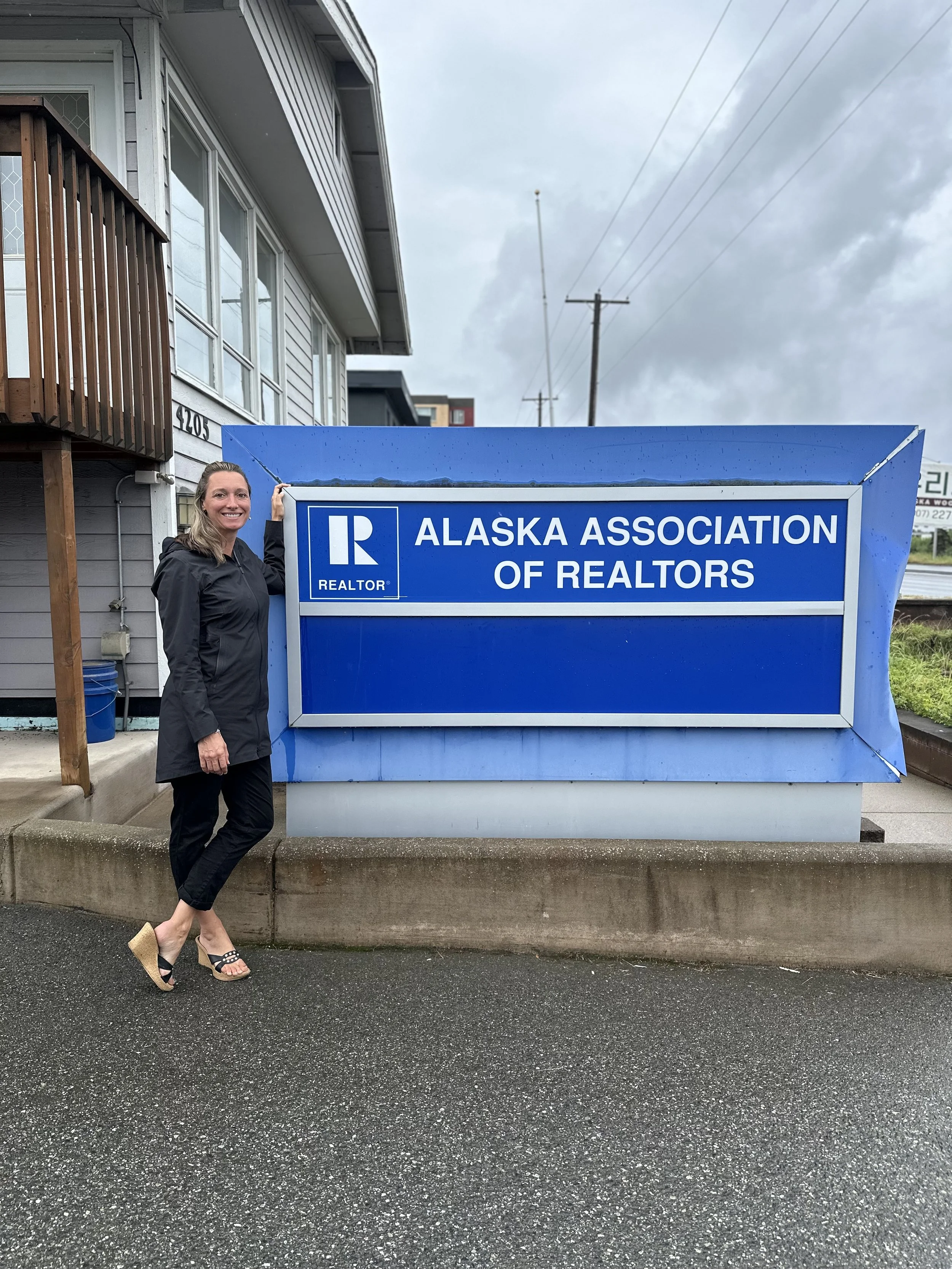 Jennifer Thompson standing in front of a blue Alaska Association of Realtors sign.