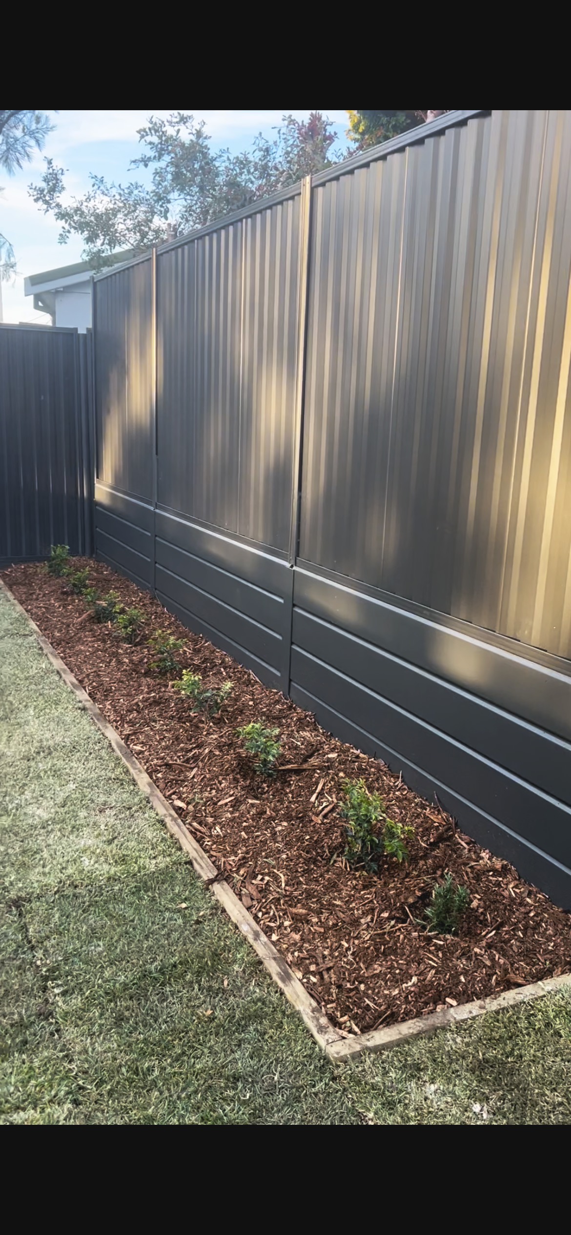 A new steel fence with horizontal slats above a landscaped garden bed with small plants, next to a grass lawn.