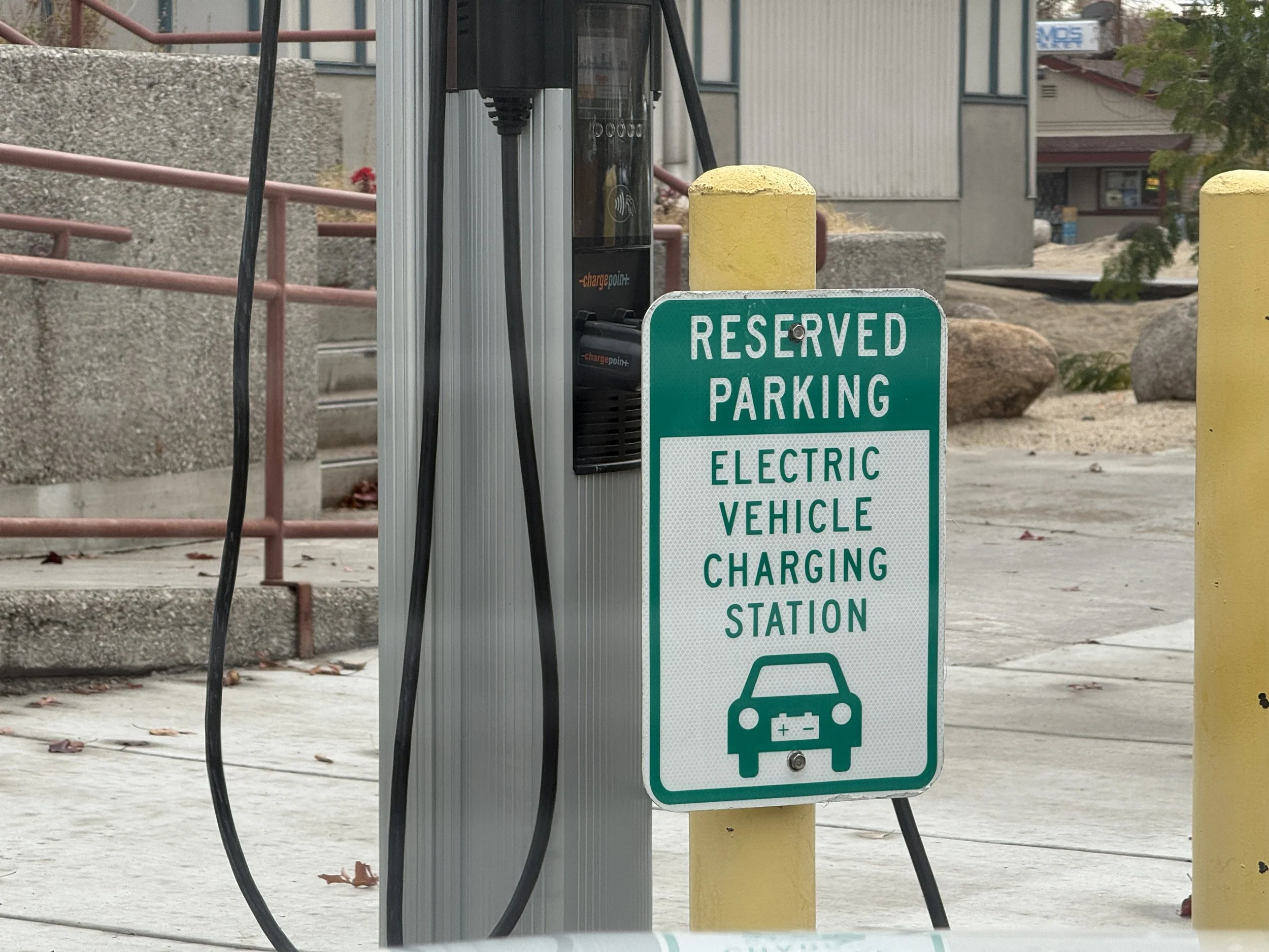 Una señal en un bolardo amarillo que dice: Aparcamiento reservado, estación de carga de vehículos eléctricos.