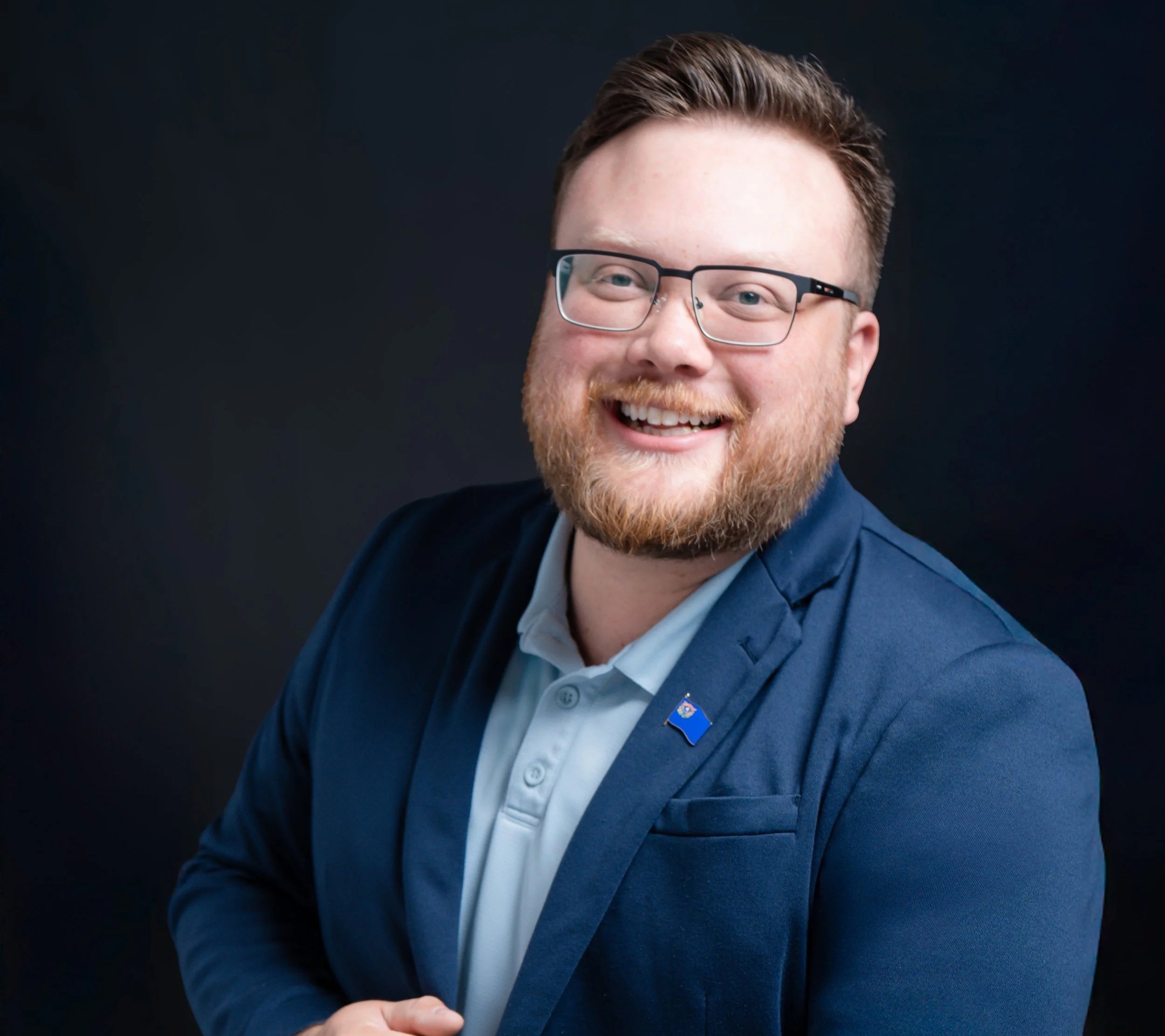 Hunter Rand, candidate for Sparks City Council, Ward 2, poses for a formal portrait in a light blue shirt and navy blue blazer, featuring a Nevada flag lapel pin.