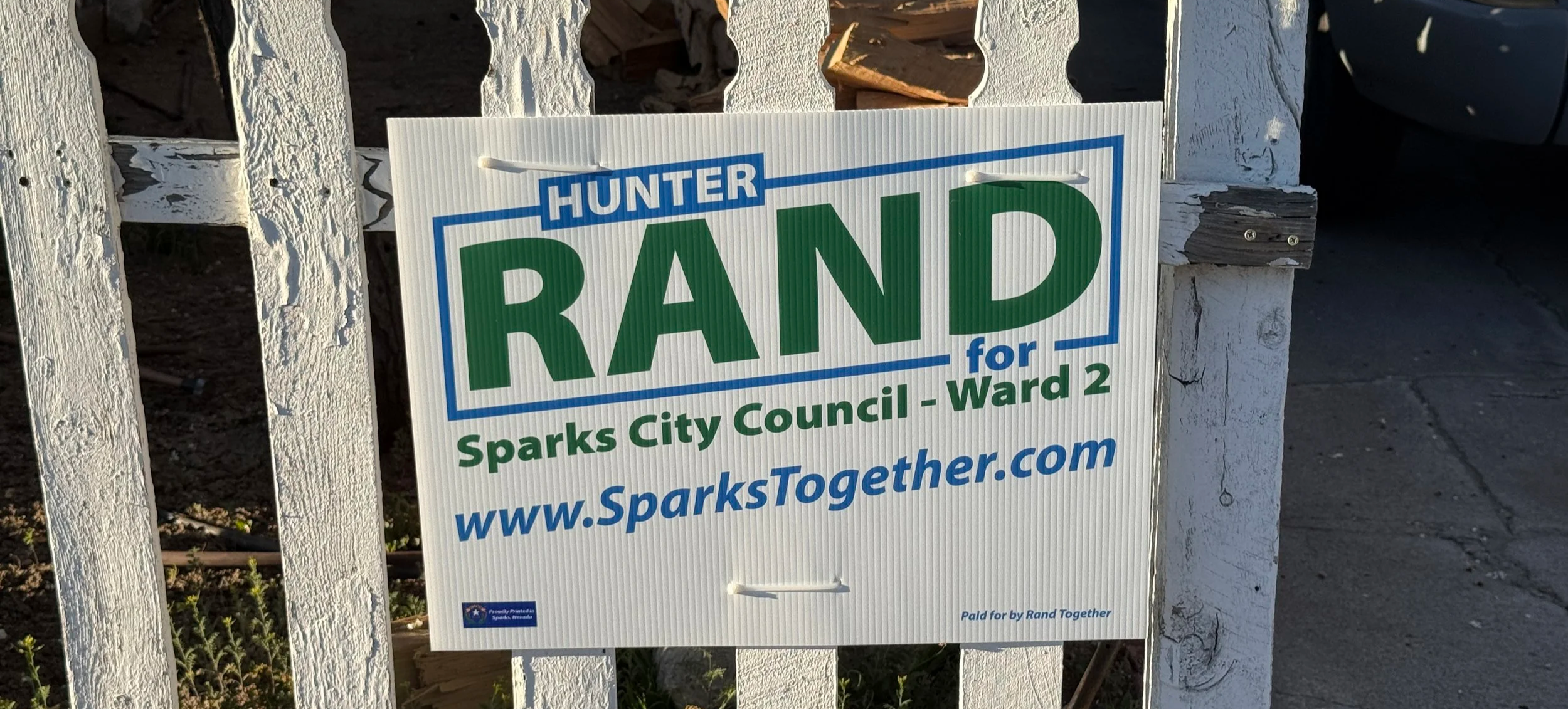 A small Rand Together yard sign attached to a white picket fence in Sparks, Nevada.