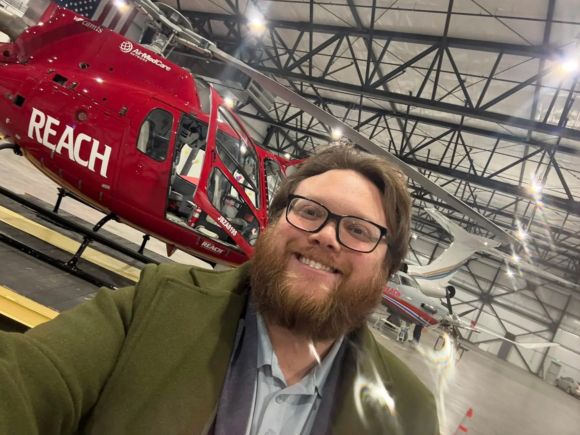 Hunter Rand stands in a hangar in front of a red REACH medical helicopter.