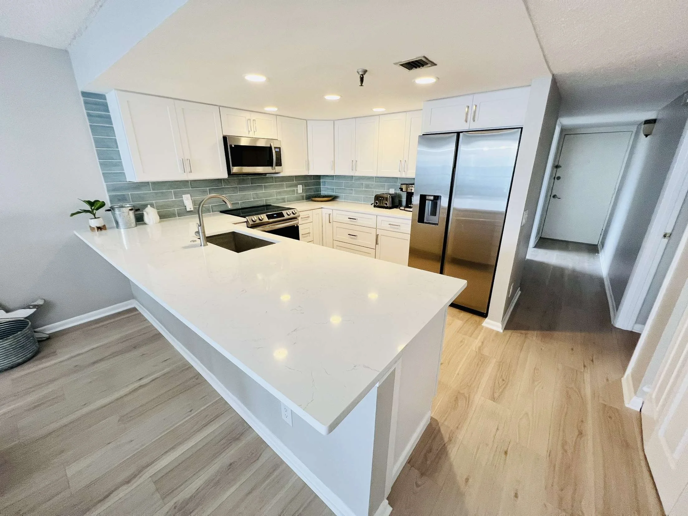 Modern kitchen with white cabinets, stainless steel appliances, marble countertop, and light wood flooring.