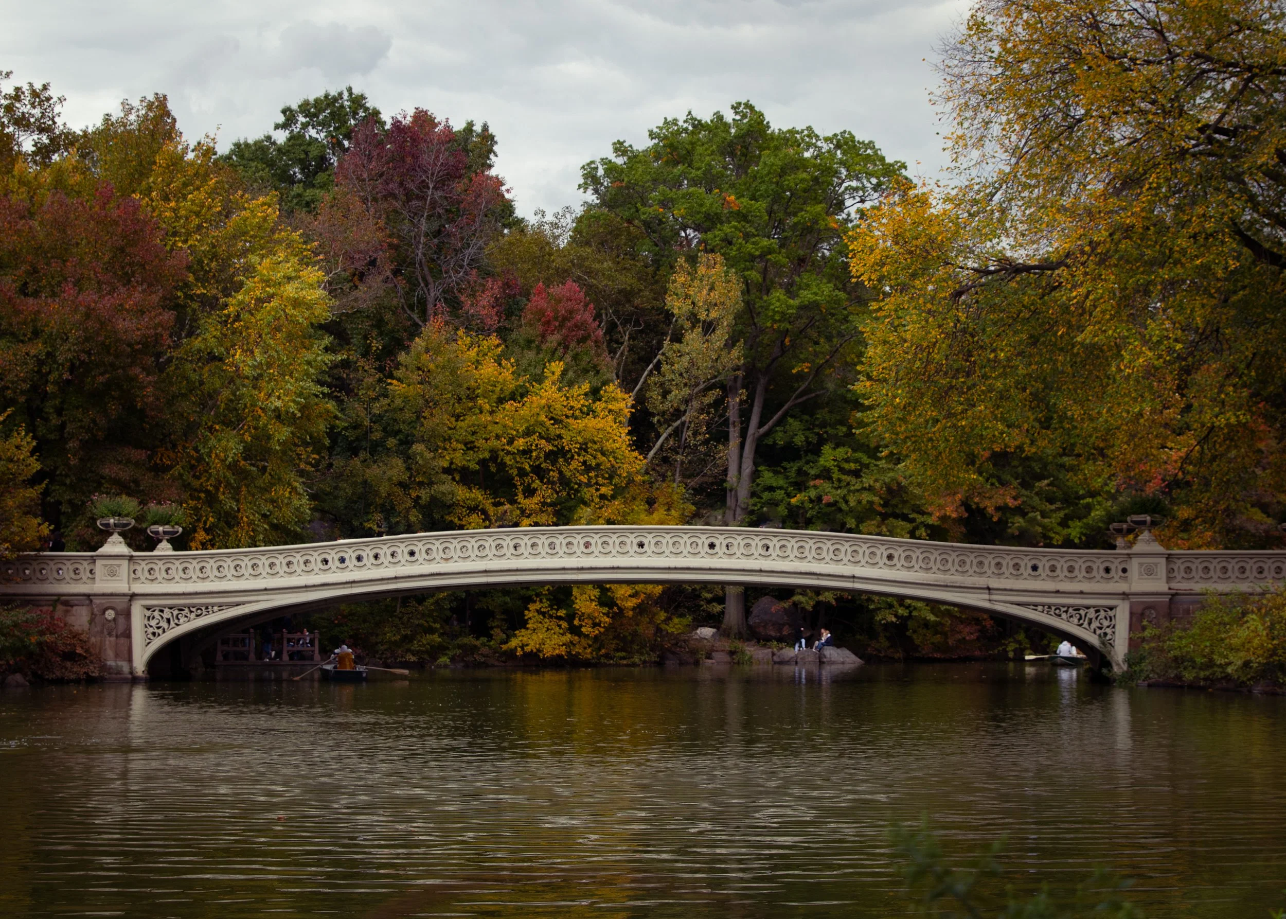 A decorative white bridge crossing a river with trees in fall colors in the background