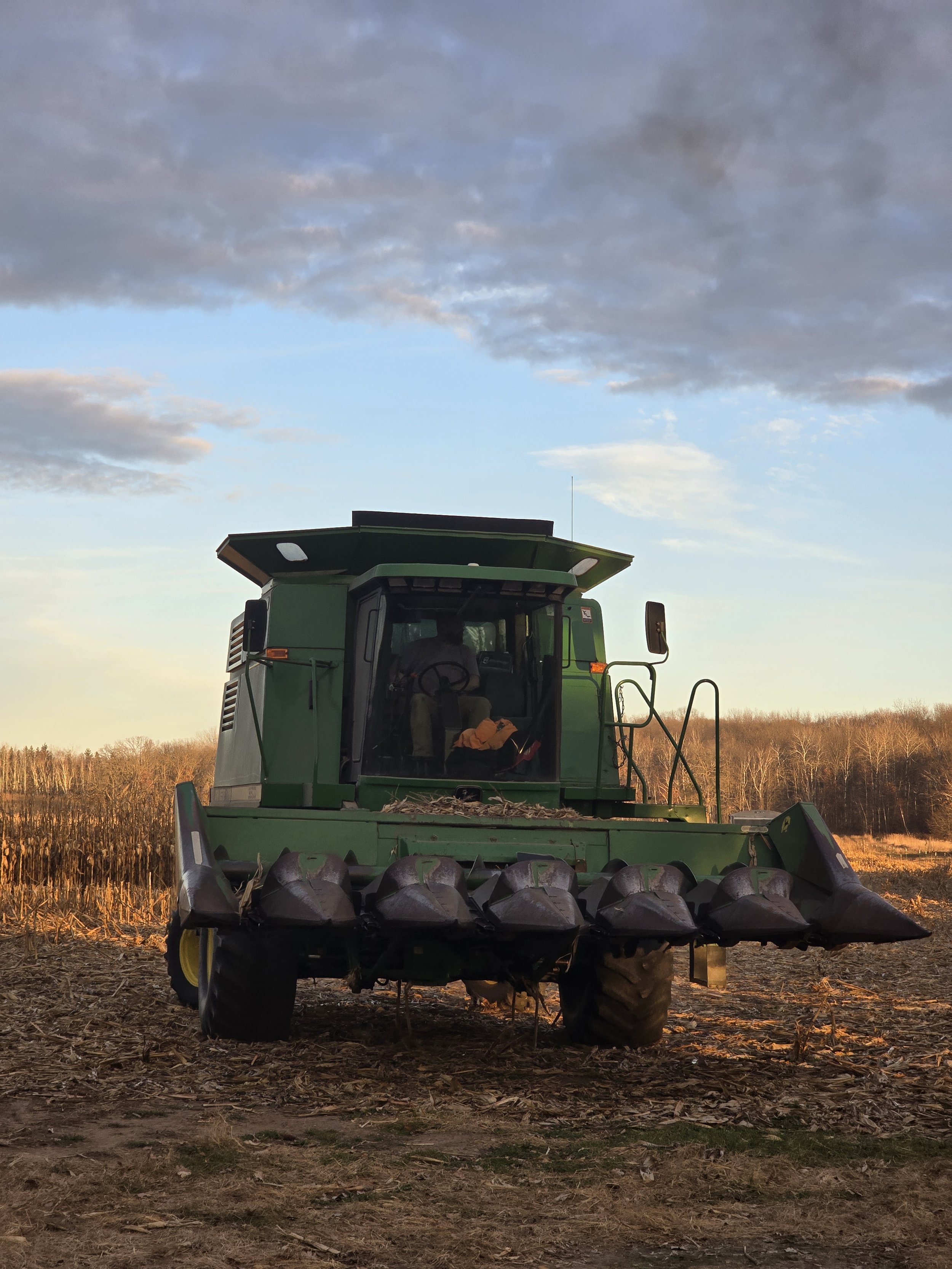 A combine harvester in a harvested field during sunset with a blue sky and scattered clouds.