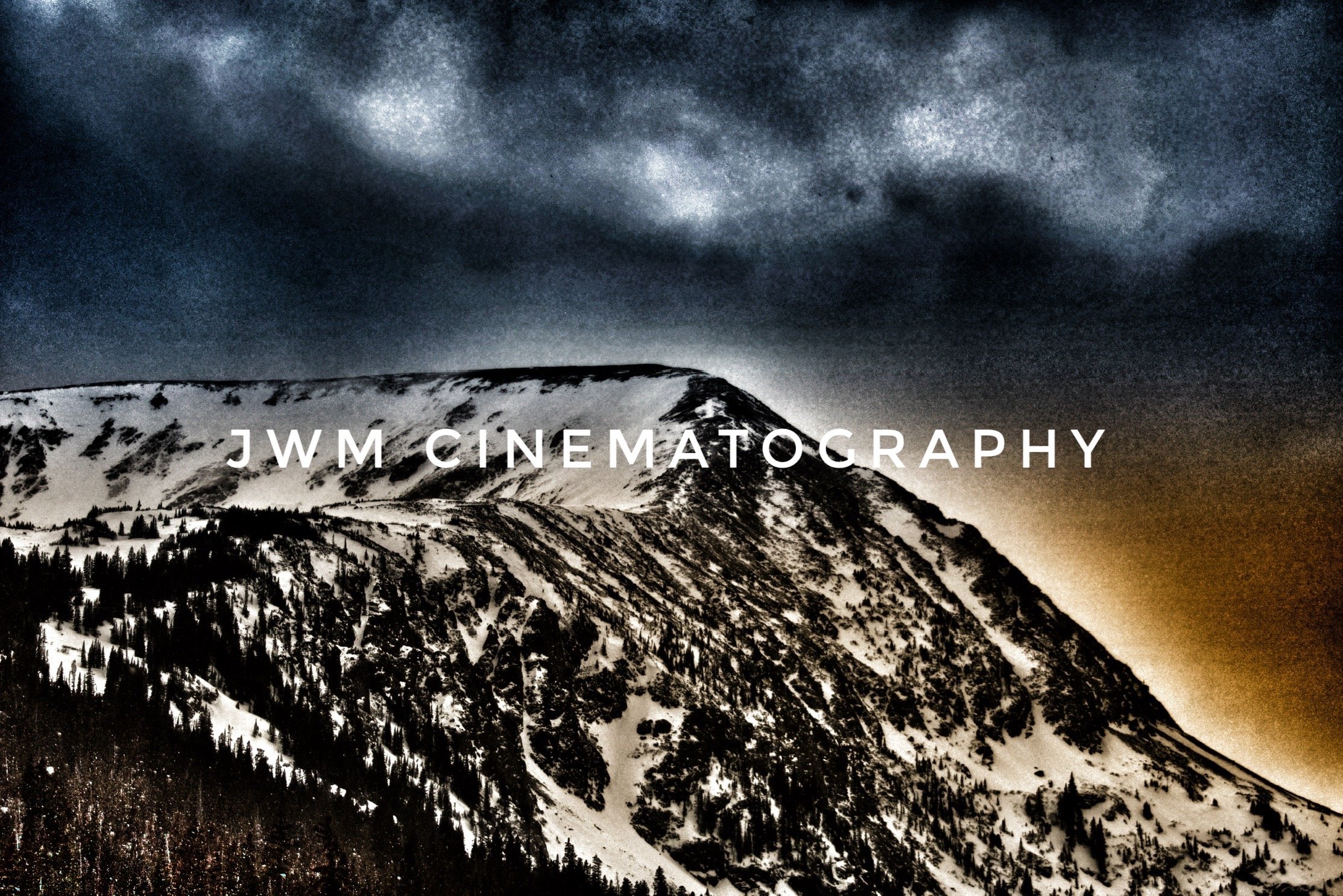 Snow-covered mountain under dramatic cloudy sky with text "JWM Cinematography."