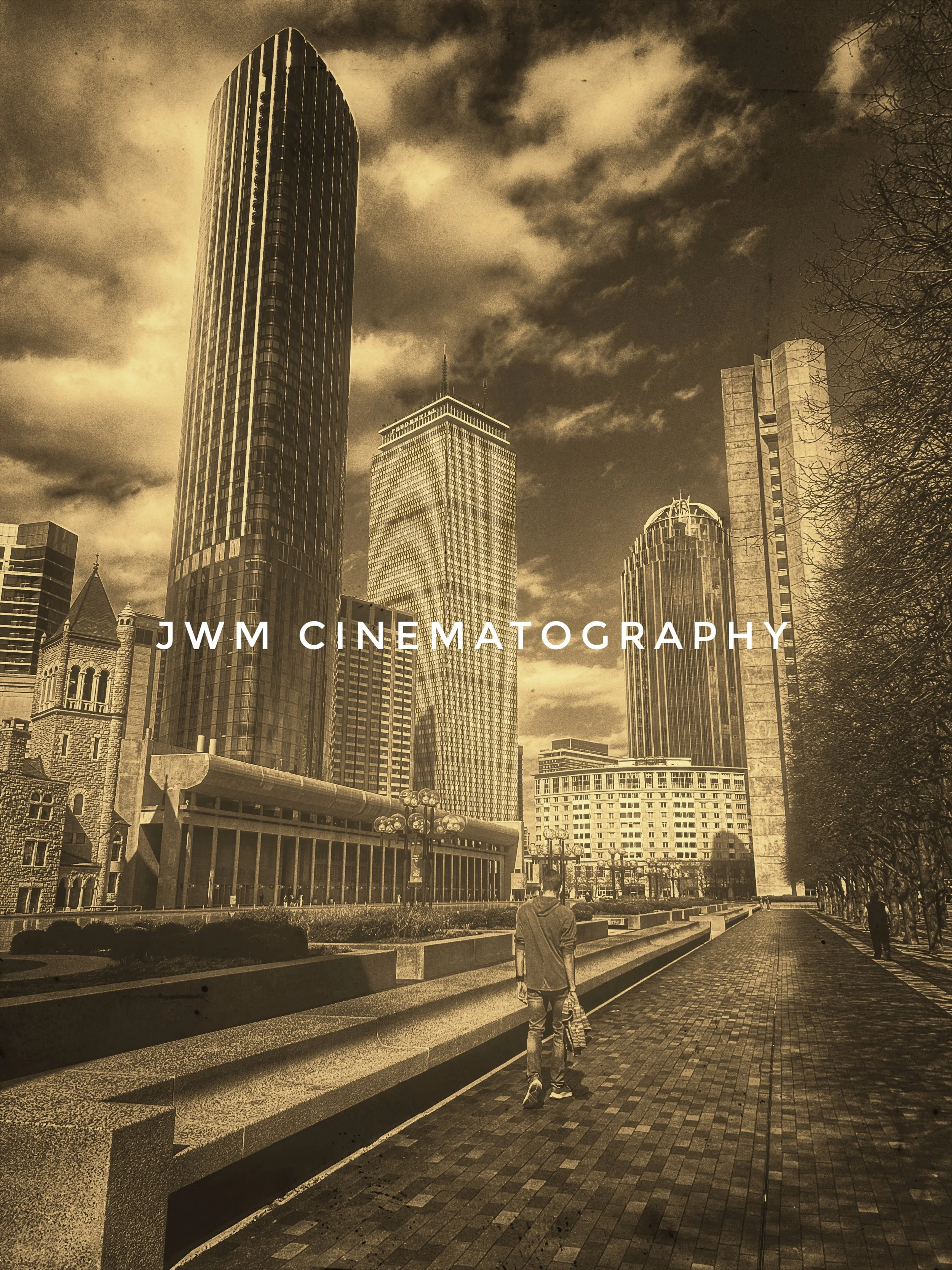 Sepia-toned image of a cityscape with tall buildings and a person walking on a paved path.