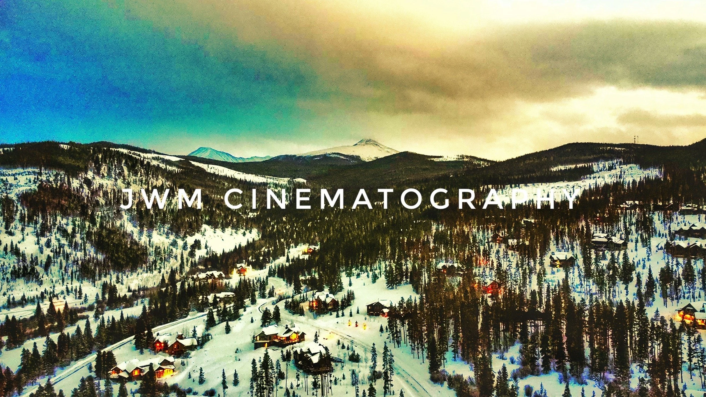 Snow-covered mountainous landscape with trees, scattered houses, and "JWM Cinematography" text overlay.