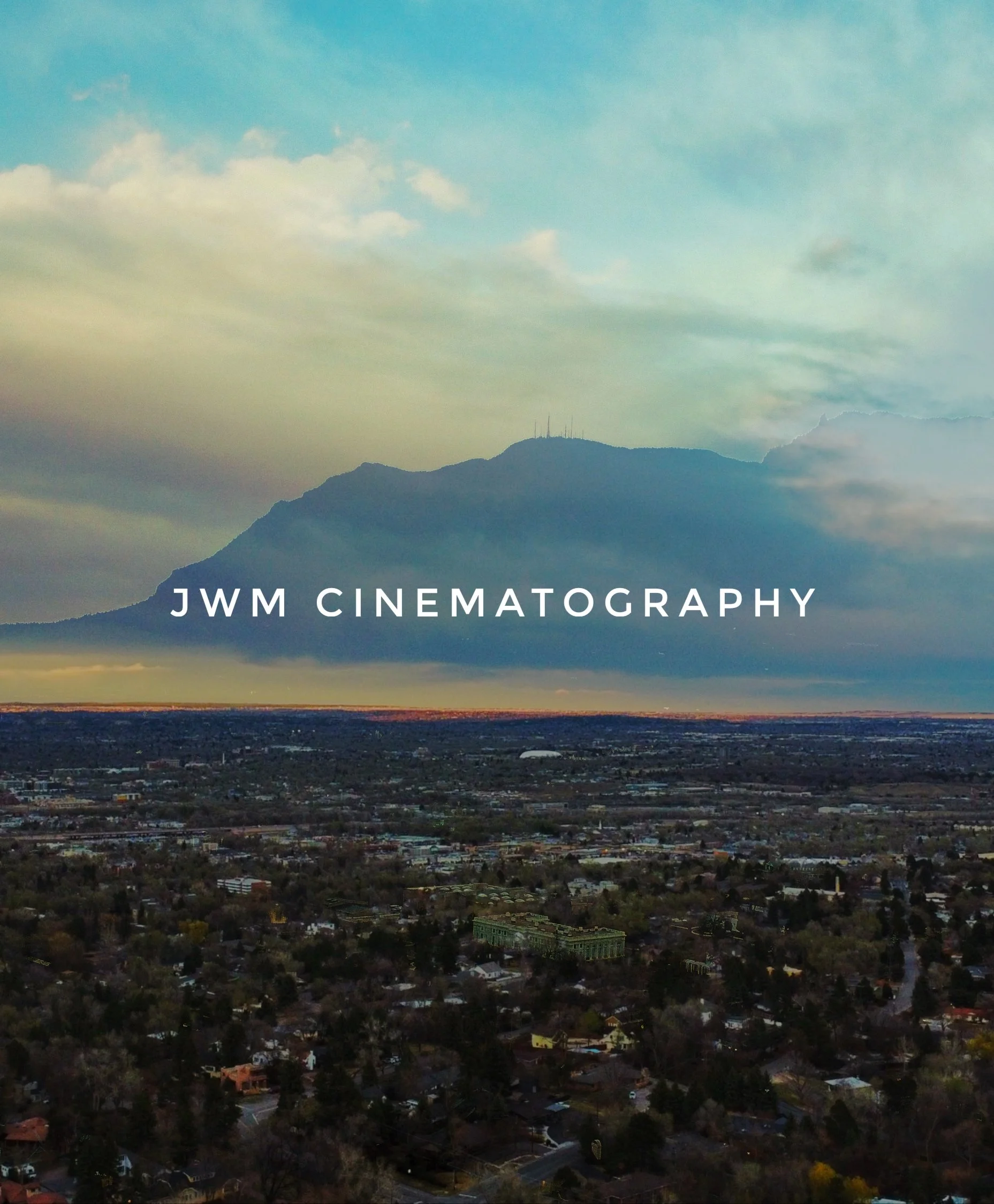Aerial view of a cityscape with a large mountain in the background, overlaid with the text 'JWM Cinematography'.