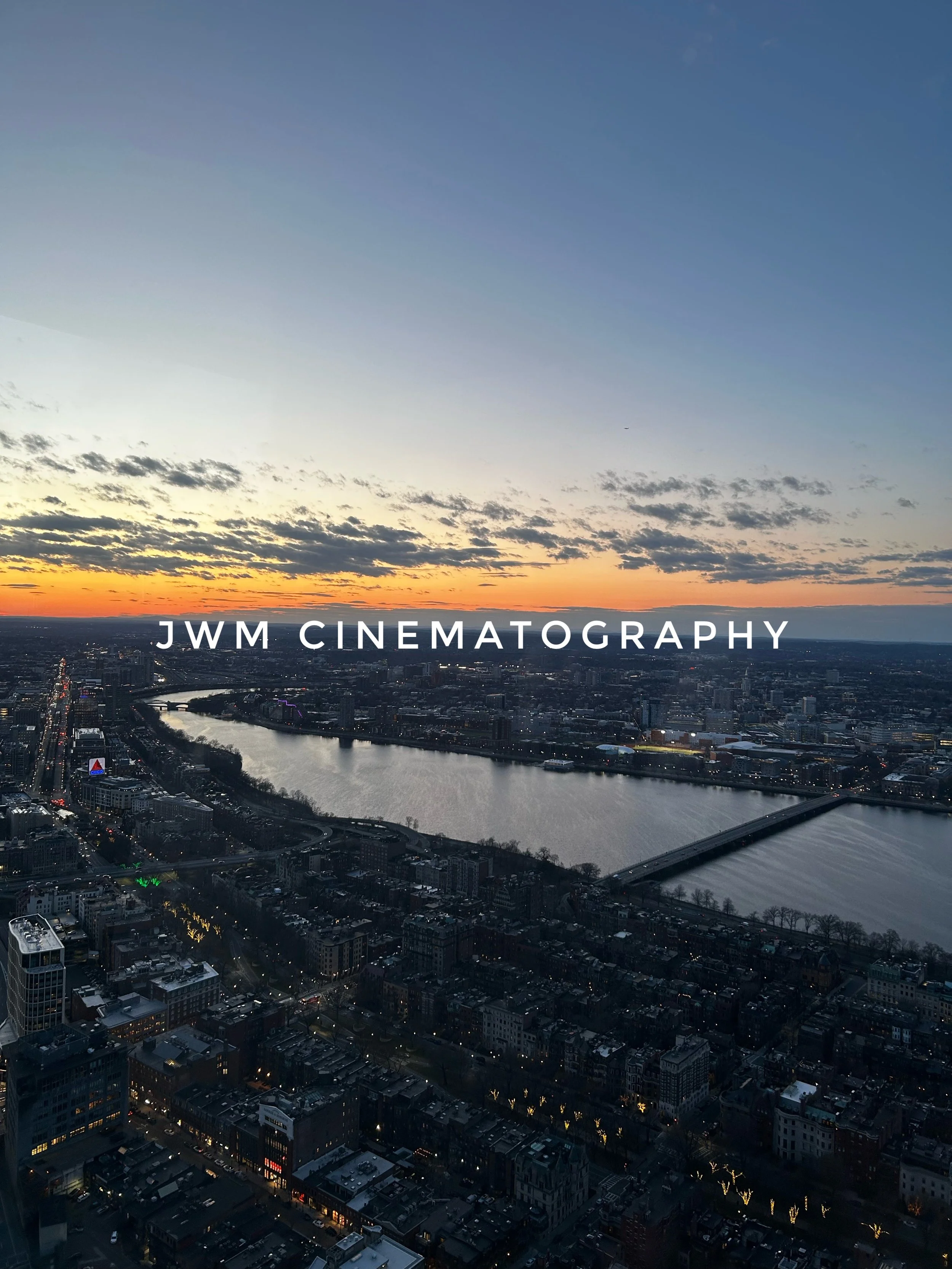 Cityscape view at dusk with a river and bridge, featuring "JWM Cinematography" text overlay.