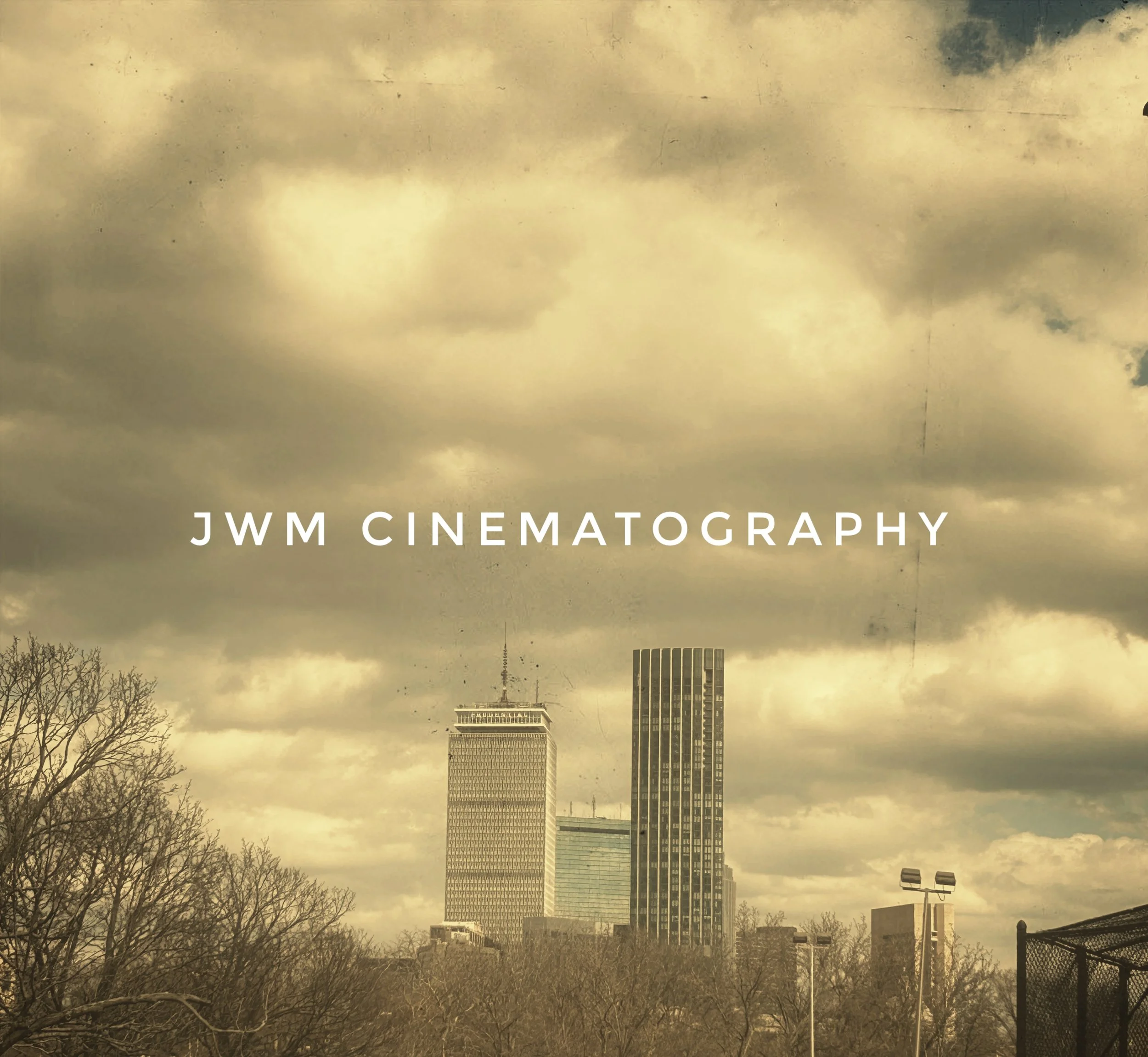 Skyline with tall buildings under cloudy sky and text "JWM Cinematography" overlaid.