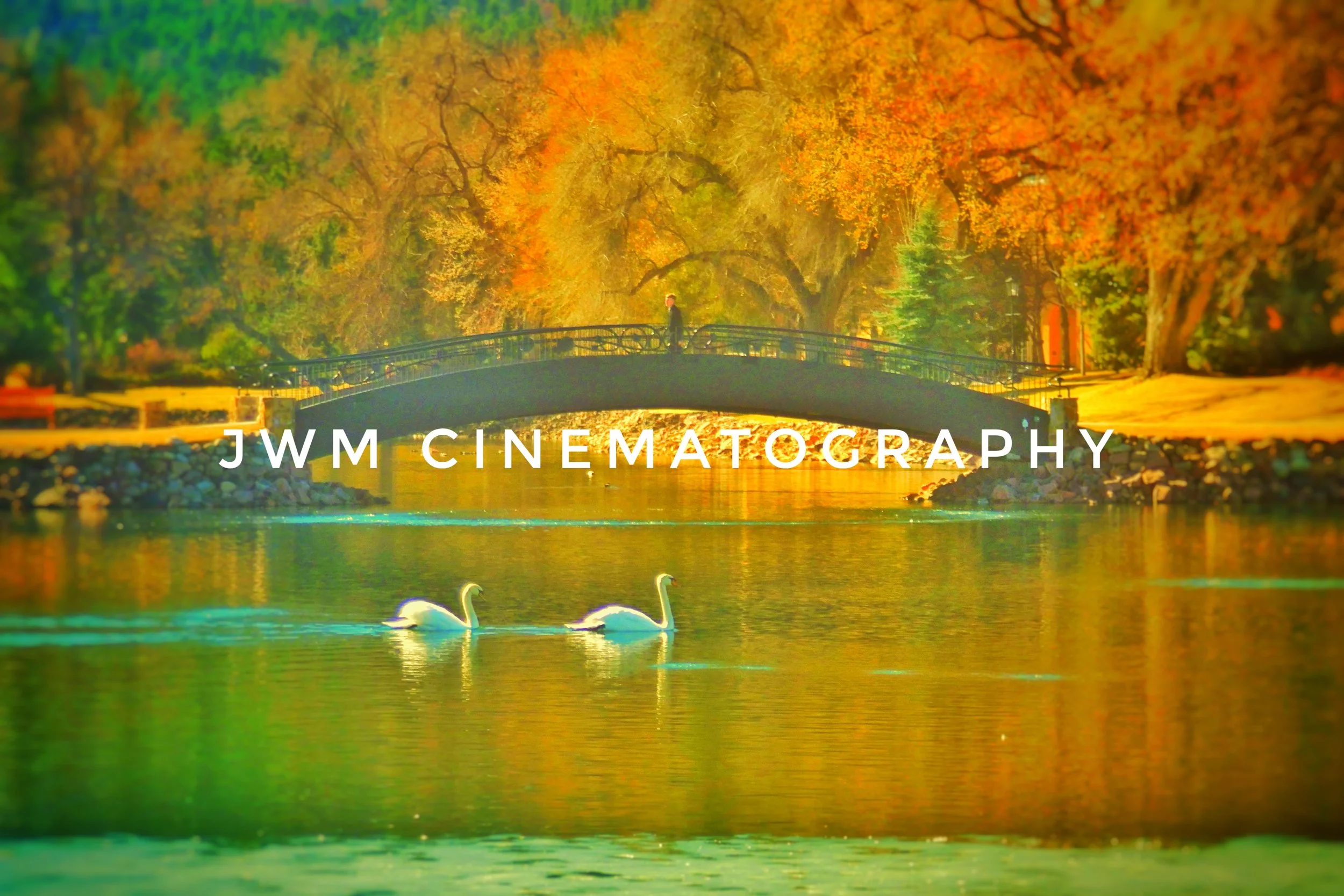 Two swans on a lake with a bridge and autumn trees in the background, "JWM Cinematography" text overlaid.