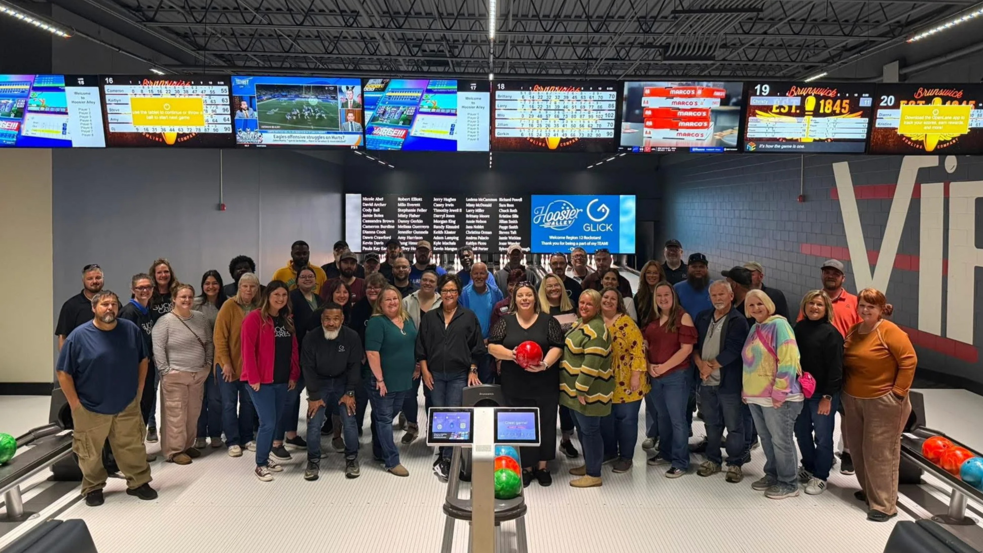 Group of people in a bowling alley, some holding bowling balls, standing in front of their customized LED wall during a VIP Section Rental.